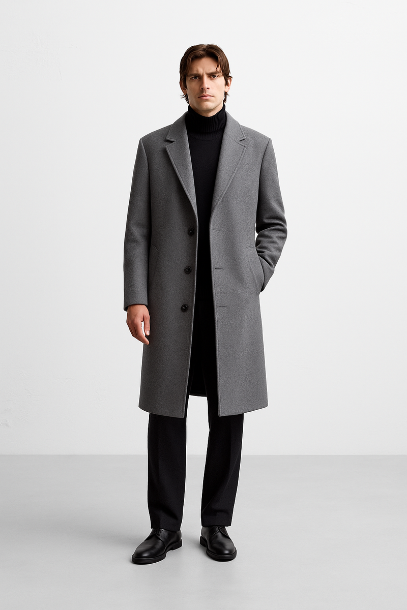 Um homem posa diante de fundo branco, usa o Casaco Sobretudo Masculino Longo Abaixo dos Joelhos da Zellum sobre suéter, calças e sapatos pretos, ressaltando conforto premium e o excelente acabamento da peça elegante.