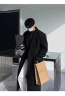 Sobretudo Coreano Masculino Longo preto com estilo minimalista, usado com calça branca e suéter escuro. Perfeito para moda masculina contemporânea.