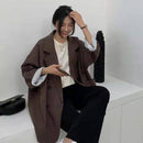 Mulher sentada vestindo blazer alongado marrom, visual casual e confortável para o dia a dia.