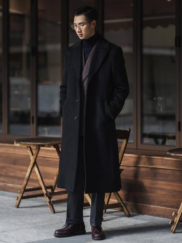 Homem usando sobretudo masculino preto elegante com cachecol vinho, calça de alfaiataria e sapatos sociais, em ambiente urbano sofisticado