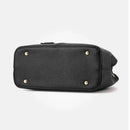 Bolsa tote preta com textura granulada e pés metálicos dourados na base.