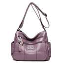 Bolsa tiracolo de couro feminina lilás com textura granulada e painéis frontais em matelassê, múltiplos bolsos com zíper e alça transversal ajustável.