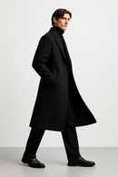 Um homem com casaco Zellum Sobretudo Masculino Longo Abaixo dos Joelhos, gola alta preta, calças e sapatos caminha com confiança contra um fundo branco liso - exalando conforto premium a cada passo.