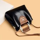 Bolsa feminina preta de couro com aba marrom e logotipo, alça ajustável