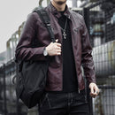 Homem com jaqueta de couro vinho, blusa preta e jeans escuros, bolsa tiracolo e colar de cruz