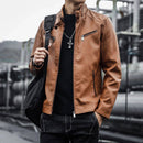 Homem com jaqueta de couro caramelo, gola alta, bolsos com zíperes, blusa preta e jeans escuro