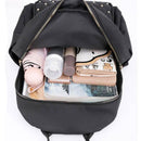 Visão superior do compartimento principal da mochila feminina pequena de nylon preta, exibindo itens como guarda-chuva, cosméticos, carteira e livro, demonstrando sua capacidade de armazenamento.