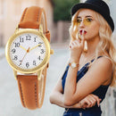 Relógio dourado com pulseira de couro tan e mulher usando óculos amarelos e chapéu preto