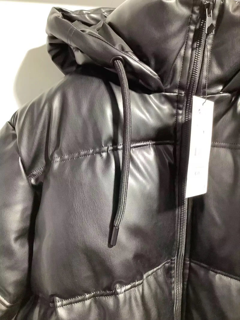 Close-up de uma Jaqueta Puffer Feminina para Inverno da Zellum. A jaqueta preta e brilhante tem costura horizontal, material de couro sintético, capuz preto com cordão, zíper visível e uma etiqueta de preço branca na gola.