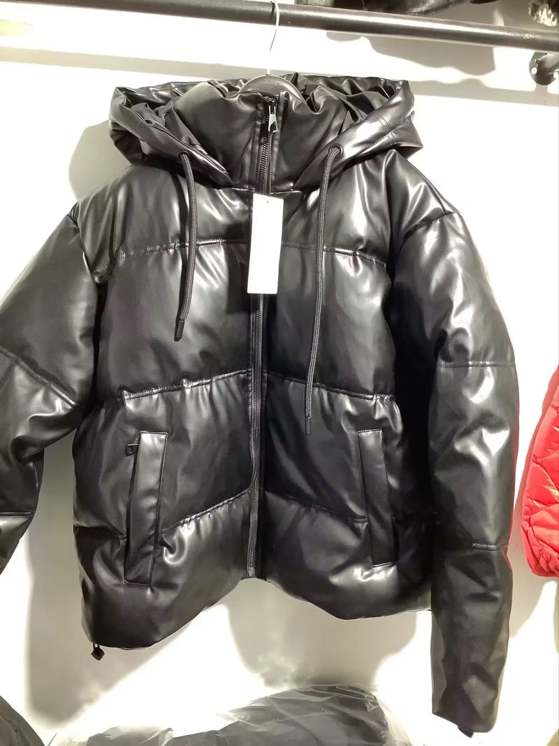 Uma Jaqueta Puffer Feminina para Inverno preta brilhante da Zellum com capuz está pendurada em um cabide contra uma parede branca. Ela apresenta um zíper frontal, bolsos laterais e uma etiqueta branca. Uma jaqueta vermelha está parcialmente visível no lado direito.
