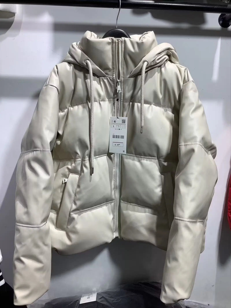 Uma Jaqueta Puffer Feminina para Inverno da Zellum na cor creme com acabamento brilhante está pendurada em um cabide preto. Essa jaqueta acolchoada tem capuz com cordões, zíper frontal, bolsos laterais e exibe uma etiqueta branca de varejo.