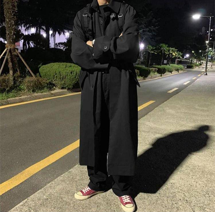 Sobretudo preto masculino com corte longo e elegante, ideal para dias frios. Combinação com tênis e look urbano noturno.