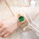 Relógio dourado com mostrador verde e pulseira de elo, usado no pulso