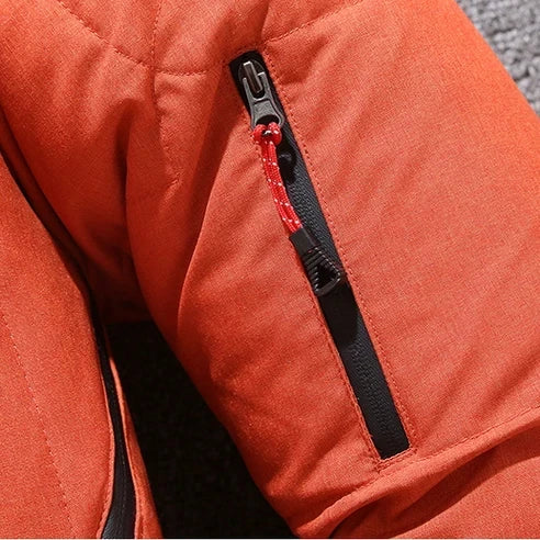 Close-up da Jaqueta Masculina Parka Acolchoada com Capuz e Zíperes Táticos laranja da Zellum, mostrando sua manga com um bolso vertical de zíper preto e cordão de puxar vermelho-branco, em um fundo cinza texturizado.