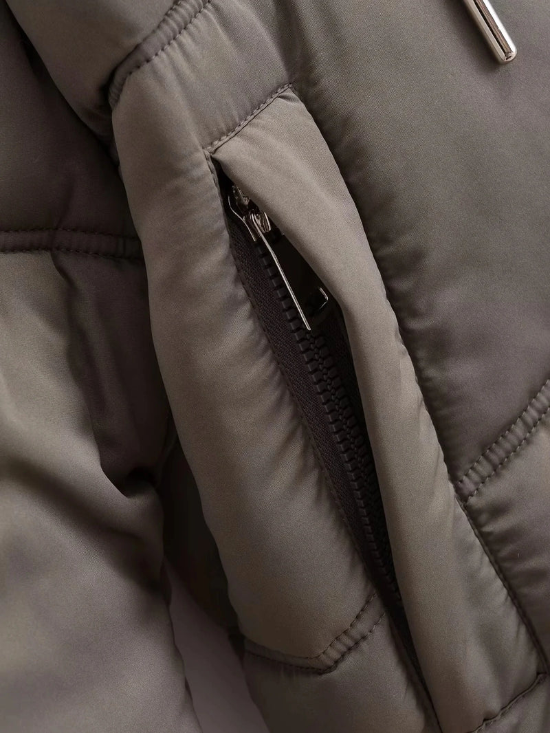 Close-up da Zellum Jaqueta Feminina Puffer para Inverno em taupe, mostrando um bolso parcialmente aberto. Seu tecido liso e brilhante e a costura detalhada enfatizam o estilo, com um zíper preto e uma aba metálica.