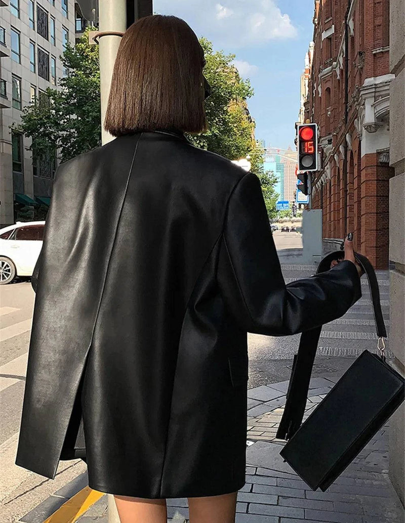 Mulher de costas usando jaqueta de couro oversized feminina preta, estilo blazer com fenda elegante na parte traseira, exibindo o caimento imponente e o luxo do couro, para um visual sofisticado nas ruas de Embu das Artes.