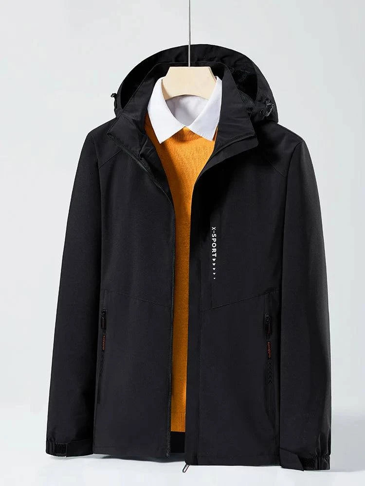 Jaqueta corta-vento preta com capuz embutido, aberta revelando uma camisa social branca e um suéter laranja por baixo. Design versátil para sobreposição, combinando funcionalidade e elegância discreta.