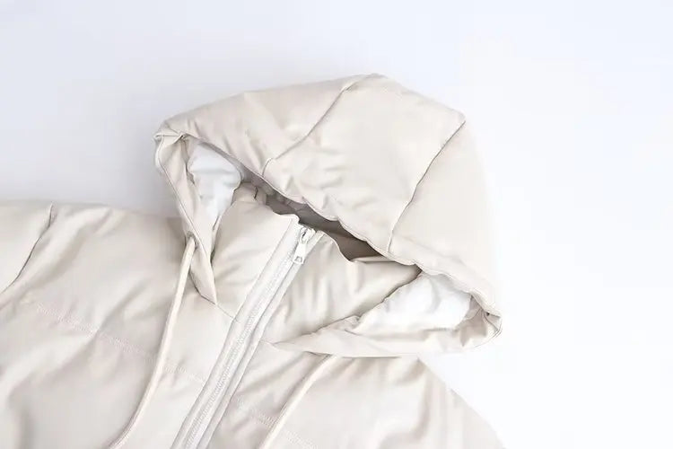 Um close-up mostra a parte superior da Jaqueta Puffer Feminina para Inverno da Zellum em bege claro sobre fundo branco, com capuz acolchoado, costuras visíveis e frente parcialmente aberta que revela o forro interno branco.