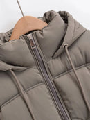 Jaqueta puffer cinza feminina com acolchoado, zíper frontal e capuz ajustável em cabide de madeira.