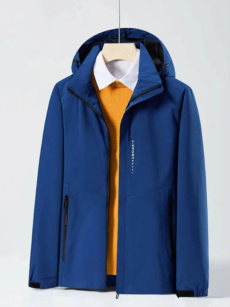Jaqueta corta-vento azul royal com capuz embutido, aberta revelando uma camisa social branca e um suéter laranja por baixo. Combinação vibrante e funcional para um estilo dinâmico e versátil.
