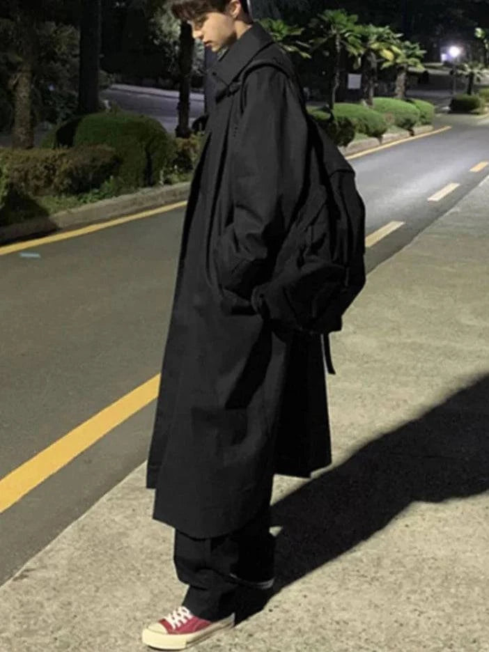 Casaco longo masculino preto com corte reto e caimento elegante, perfeito para outono/inverno. Look urbano com mochila preta.