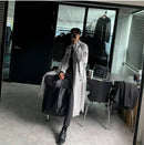 Homem usando trench coat longo cinza claro com bolsa tote em ambiente de escritório
