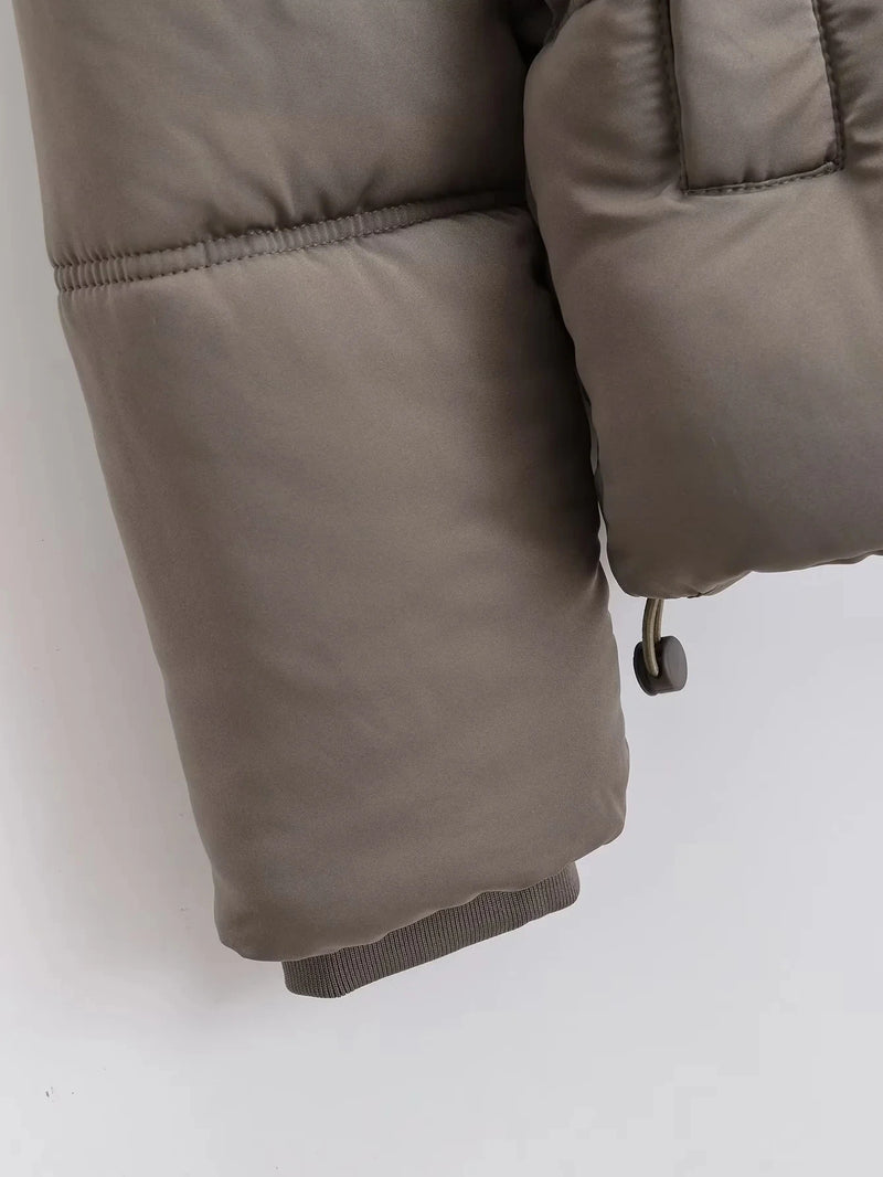 Close-up da manga de uma Jaqueta Feminina Puffer para Inverno da Zellum em taupe, com tecido fosco liso, punho elástico, bolso acolchoado com costura visível e fecho com cordão. Fundo claro e liso.