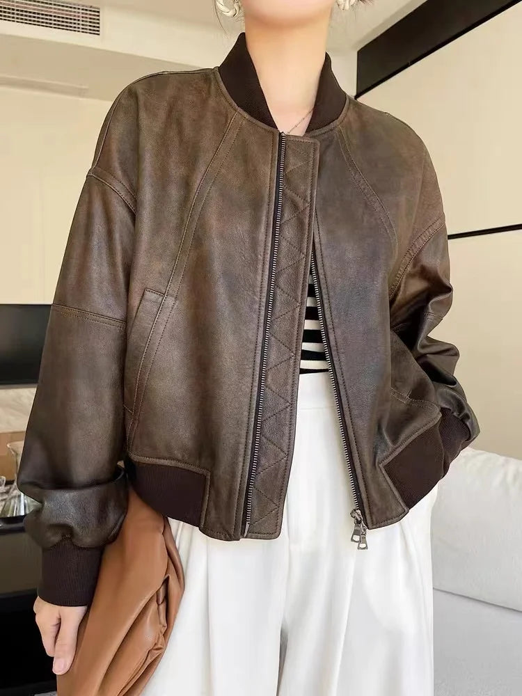 Uma pessoa usa a Zellum Jaqueta Feminina de Couro Urban com gola e punhos pretos sobre uma blusa listrada e calça branca de cintura alta, segurando uma bolsa marrom em um ambiente moderno e de tons neutros.
