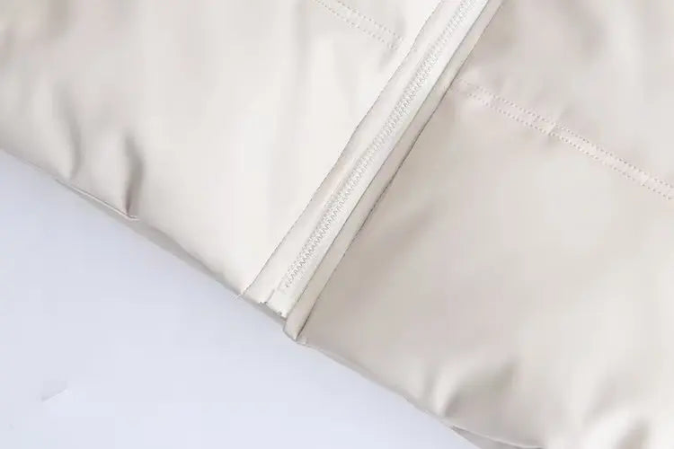 Close-up do tecido bege claro da Jaqueta Puffer Feminina para Inverno da Zellum, mostrando um zíper visível e uma costura bem feita. O material é liso e levemente brilhante, o que indica uma construção de qualidade.