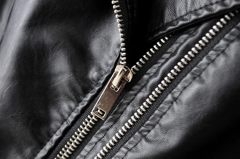 Close-up de um zíper prateado parcialmente aberto na Jaqueta de Couro Feminina Vogue Noir da Zellum, destacando a costura detalhada e a textura de couro PU. O zíper metálico contrasta com a superfície lisa e levemente enrugada da jaqueta.