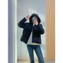 Mulher com jaqueta puffer preta, capuz e jeans em selfie