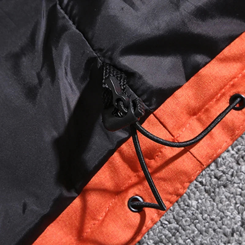 Close-up da Zellum Jaqueta Masculina Parka Acolchoada com Capuz e Zíperes Táticos em preto e laranja, mostrando um cordão com fecho de plástico passando por ilhós de metal na bainha laranja, contra um fundo cinza com textura de carpete.