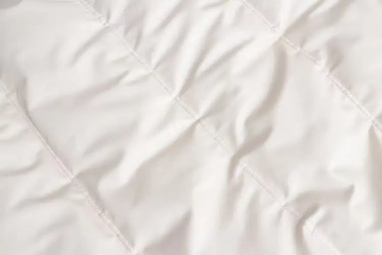 Close-up de um tecido acolchoado branco com linhas de grade costuradas e dobras suaves, destacando a textura aconchegante da Jaqueta Puffer Feminina para Inverno da Zellum sob iluminação uniforme para uma aparência convidativa e confortável.