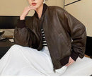 Mulher de jaqueta de couro marrom bomber, blusa listrada P&B e saia branca, em pose pensive