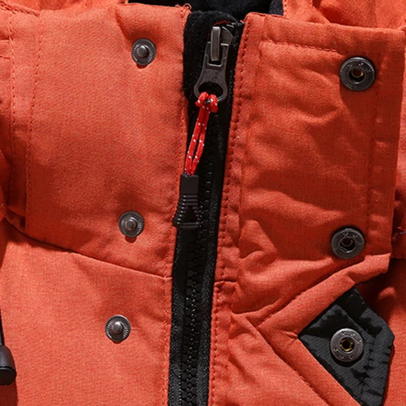 Close-up da Jaqueta Masculina Parka Acolchoada com Capuz e Zíperes Táticos da Zellum em laranja, mostrando um zíper preto com cordão de puxar vermelho, botões de pressão pretos e um pequeno detalhe de tecido preto ao lado do zíper. A textura do tecido e a costura são visíveis.