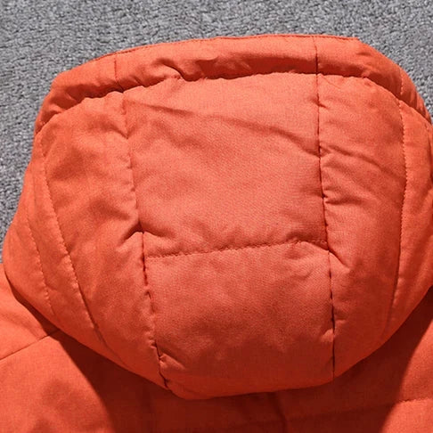 Close-up da Jaqueta Masculina Parka Acolchoada com Capuz e Zíperes Táticos laranja da Zellum, mostrando seções acolchoadas quadradas e retangulares costuradas em tecido macio e de qualidade, exibidas em um tapete cinza.