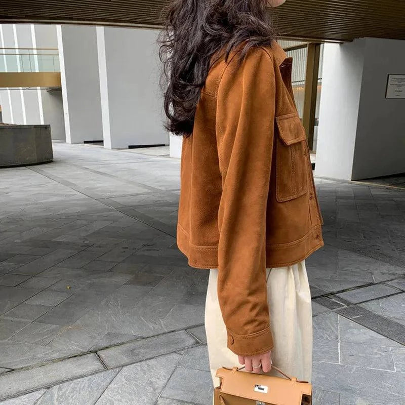 Mulher de perfil usando jaqueta feminina de pelo de cabra Hircus na cor caramelo, com bolsos de aba e botões no punho, combinada com calça clara e bolsa, exibindo um luxo sutil e exclusivo, perfeito para o estilo elegante de Embu das Artes.