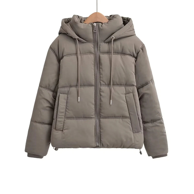 A Zellum Jaqueta Feminina Puffer para Inverno em marrom claro apresenta zíper frontal, dois bolsos laterais, capuz com cordões, costura horizontal e mangas longas. Exibida em um cabide de madeira contra um fundo branco liso.