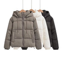 Três jaquetas puffer femininas cinza, branca e preta em cabides de madeira com capuz e zíper frontal
