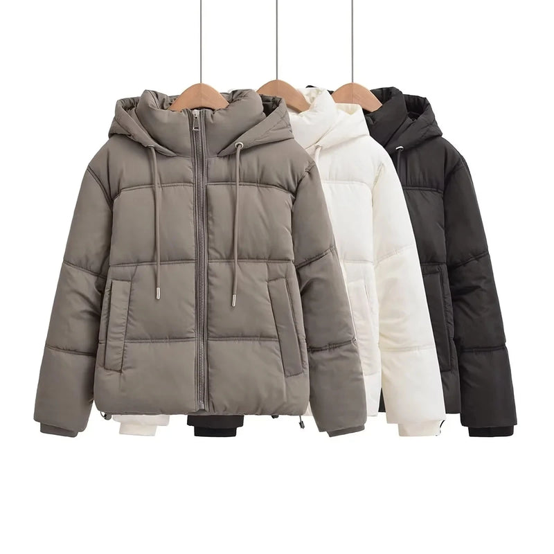 Três jaquetas Zellum Jaqueta Feminina Puffer para Inverno nas cores cinza, branca e preta penduradas em cabides de madeira. Cada uma tem um capuz com cordões, zíper frontal e dois bolsos para aquecimento e estilo.
