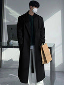 Sobretudo Coreano Masculino Longo preto com caimento sofisticado, usado com calça branca e suéter escuro. Perfeito para moda urbana e casual chique.