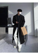 Sobretudo Coreano Masculino Longo preto em look casual com calça branca e sacola de compras. Ideal para composições modernas e práticas no inverno.