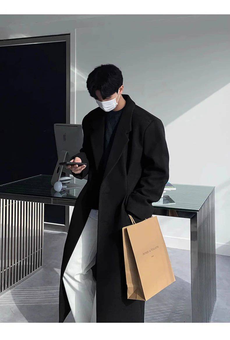 Sobretudo Coreano Masculino Longo preto com estilo minimalista, usado com calça branca e suéter escuro. Perfeito para moda masculina contemporânea.
