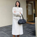 Mulher usando sobretudo longo branco com botões e bolsa preta tiracolo