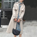 Mulher vestindo trench coat bege longo sobre vestido floral azul com bolsa preta