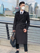 Sobretudo masculino Zellum Frost Elite preto, longo, com cinto amarrado, sobre camisa e gravata, em ambiente urbano com rio e prédios modernos.