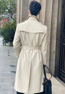Homem de costas usando trench coat bege comprido com cinto ajustado e gola larga.