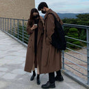 Casal em sobretudos marrons com cinto observando telefone em varanda com vista para montanhas
