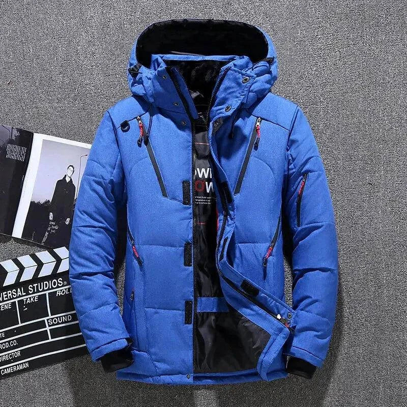 Jaqueta masculina parka acolchoada azul royal com capuz, múltiplos bolsos frontais com zíperes vermelhos e pretos, e fechamento com botões de pressão e zíper, em um fundo que remete a um estúdio de cinema. Design vibrante e funcional para um estilo de alta performance no clima de Embu das Artes.
