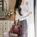Mulher com bolsa de couro vinho e alças marrons, blusa branca e saia xadrez cinza